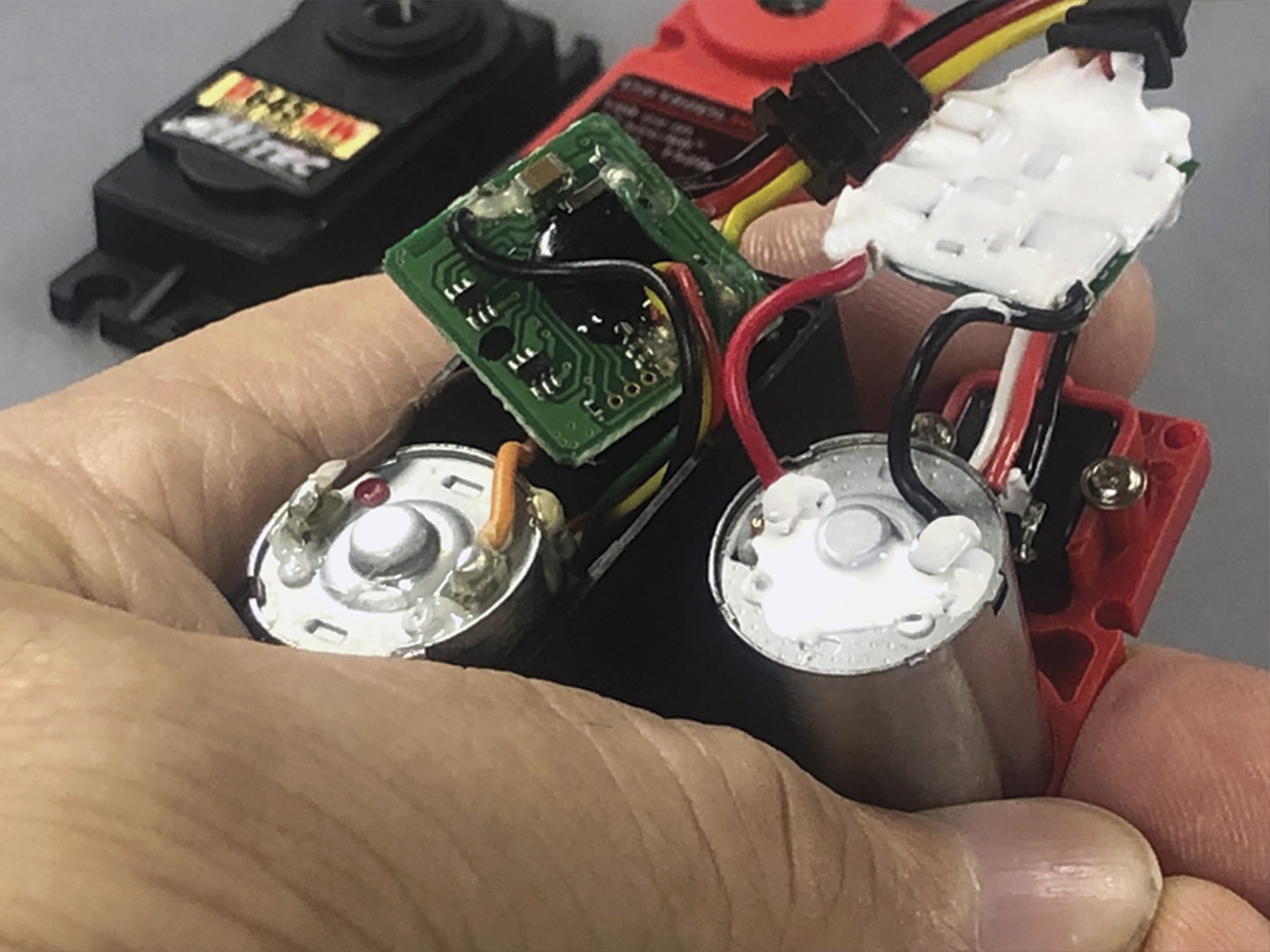 Close up of a hand holding both Hitec and ProModeler DC-motor equipped servos